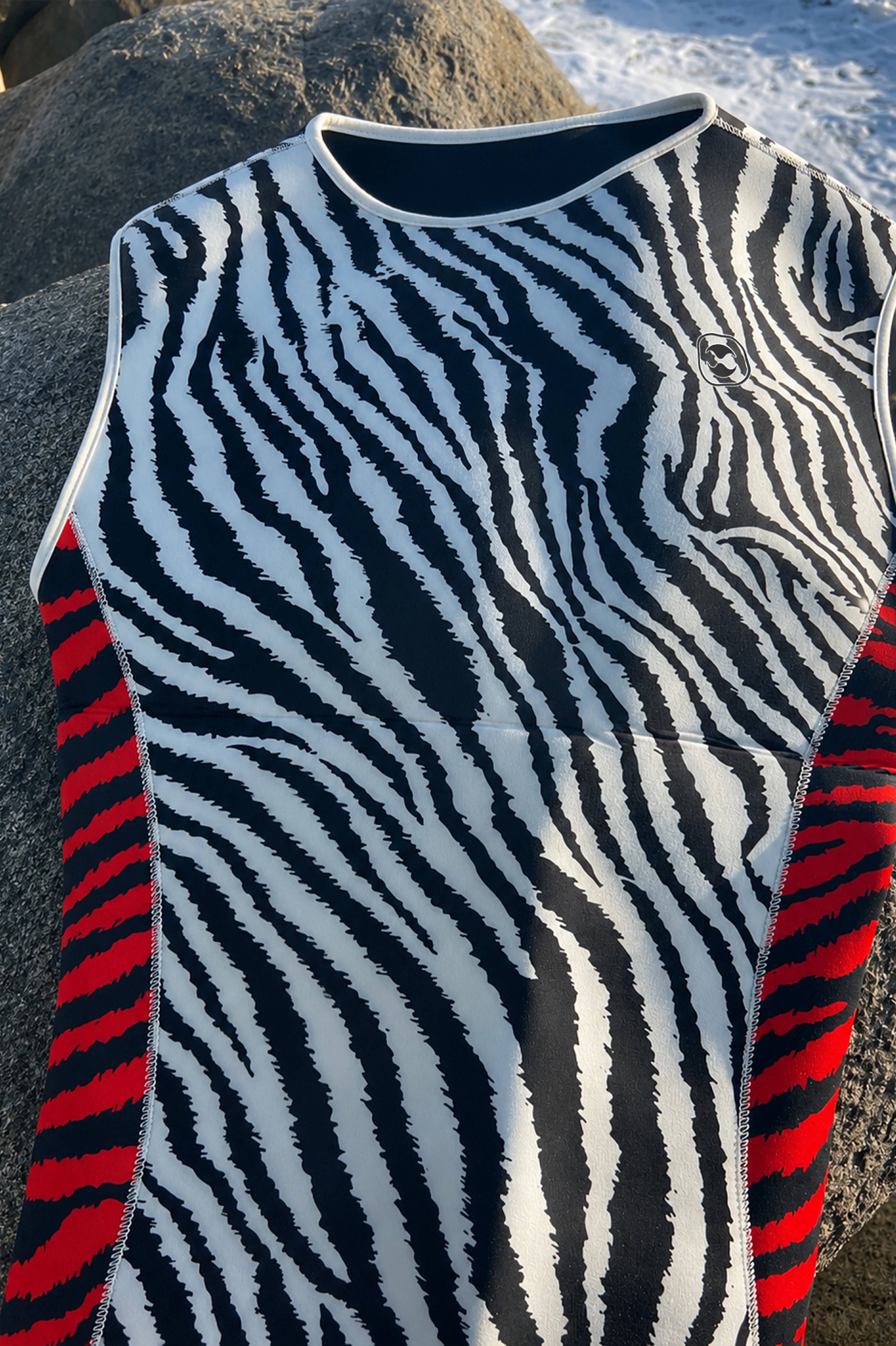 Men's Custom Neoprene Vest: A sleeveless athletic top with a bold black and white zebra stripe pattern across the front and red side panels, laid outdoors on a rock with snow visible in the background.