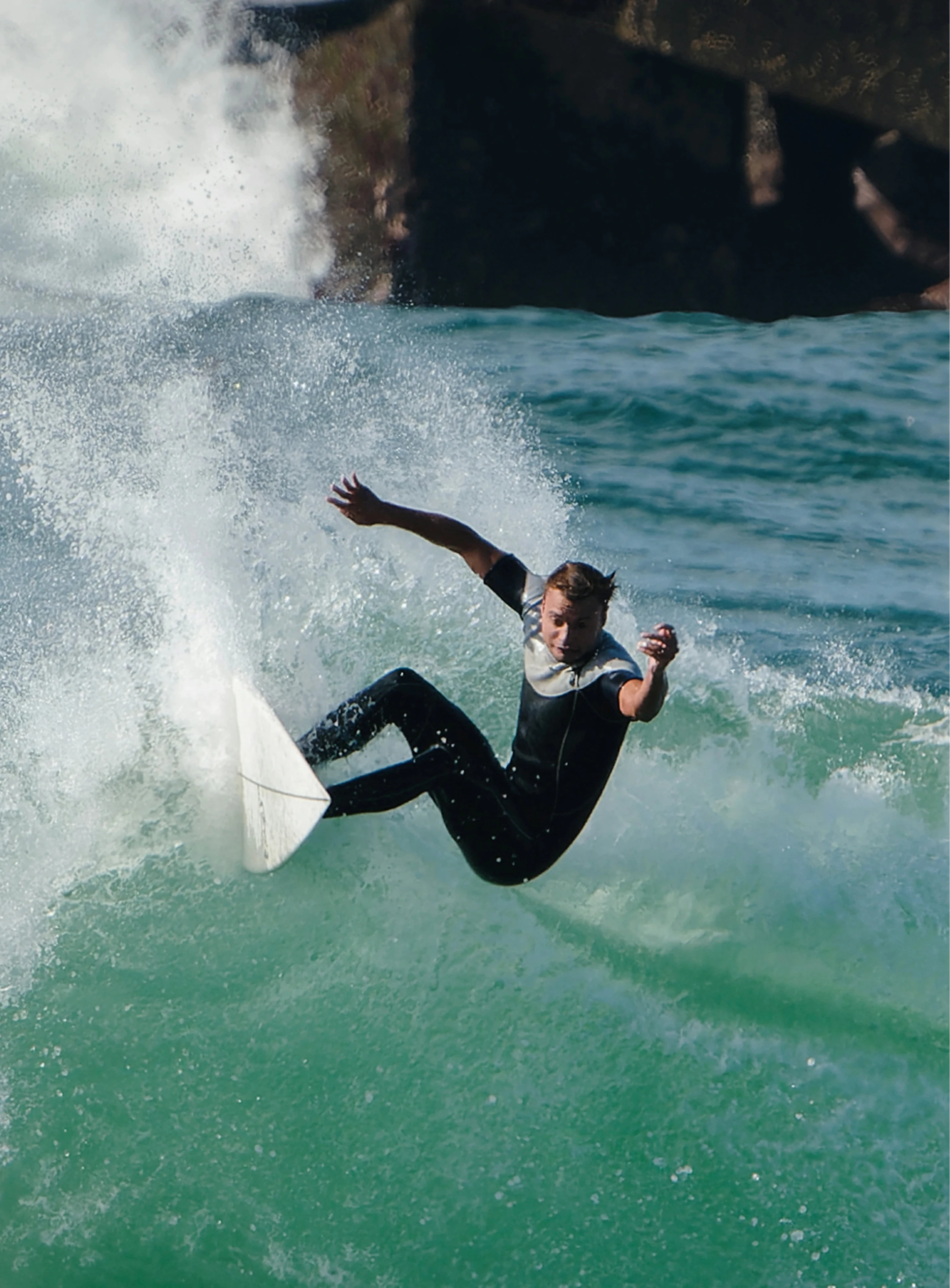 Surfer riding a wave with a rocky outcrop in the background
