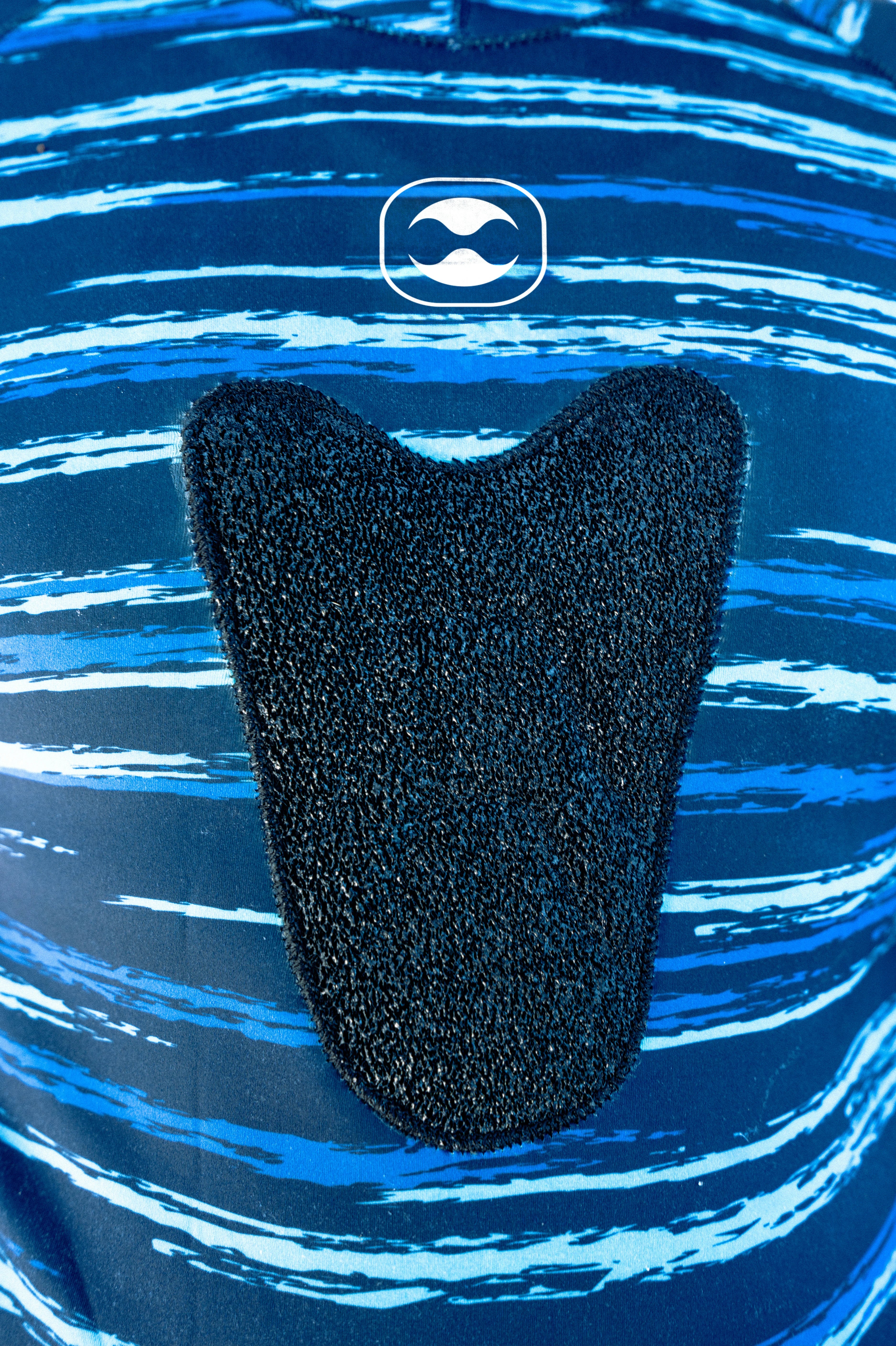 A close-up of a black textured adhesive pad applied to a blue and white patterned garment, with a white logo emblem visible above it.